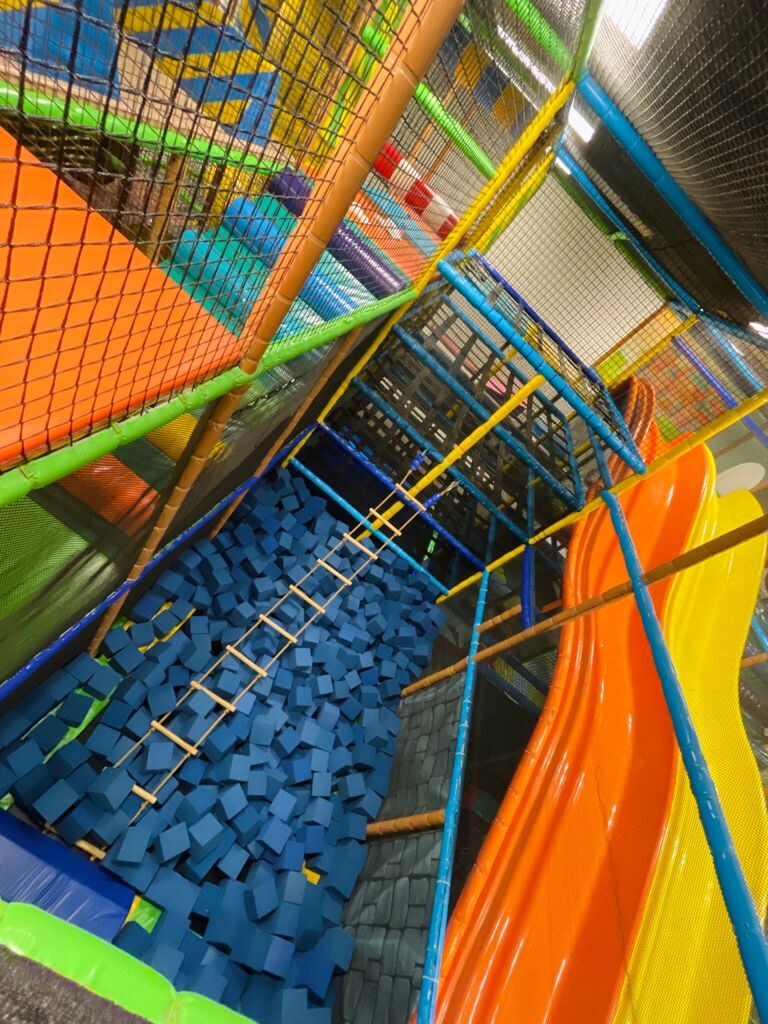 Looking down into a multi-level play structure with a foam pit, rope ladder, and slides